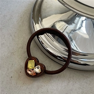 Detail of a brown elastic hair tie featuring a resin heart set with sparkling rhinestones