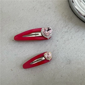 Détail de barrettes BB rouges avec strass en forme de cœur rose et gemmes brillantes