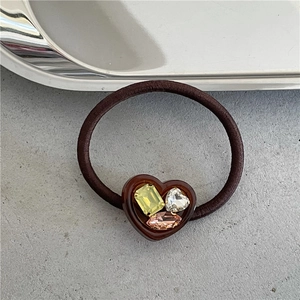 Detail of a brown elastic hair tie featuring a resin heart set with colorful rhinestones