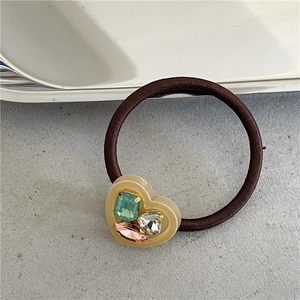 Detail of heart-shaped resin piece with colorful rhinestones on a brown elastic hair tie