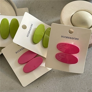 Macro detail of colorful oval hair clips in pink and green on an accessories card