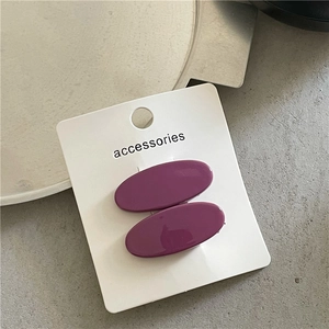 Close-up of two purple oval acrylic hair clips displayed on a minimalist white card