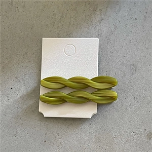 Close-up of green twisted acetate hair clips set on a display card over grey background