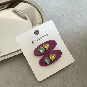 Détail de barrettes ovales mauves avec strass verts et jaunes sur carte de support