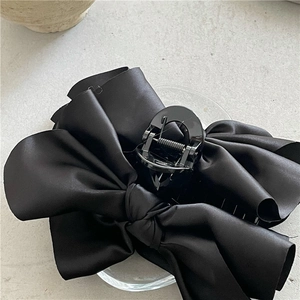 Elegant large black satin ribbon bow hair claw clip for women on a grey stone surface