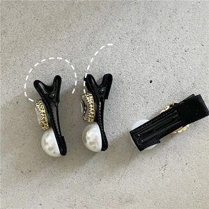 Detail von schwarzen Entenschnabel-Clips mit Kunstperlen und goldenen Reliefknöpfen