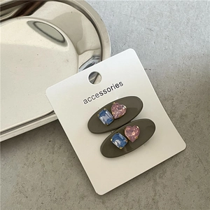Détail de barrettes ovales avec cœur rose et pierre bleue sur carte de présentation