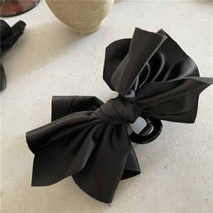 Detail of the elegant black satin ribbon bow hair claw clip showing glossy fabric texture