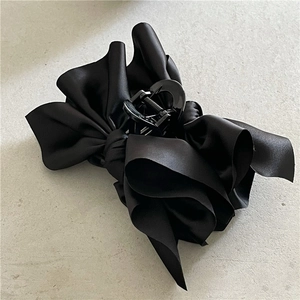 Close-up of a large black satin bow hair claw clip with glossy multi-layered fabric
