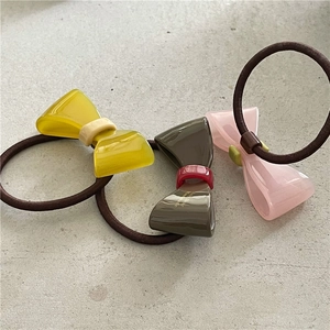 Detailansicht von drei Acetat-Haargummis mit Schleifen in Gelb, Rosa und Mokkabraun