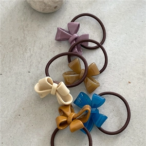 Detailed close-up of acetate bow hair ties in five colors on marble background