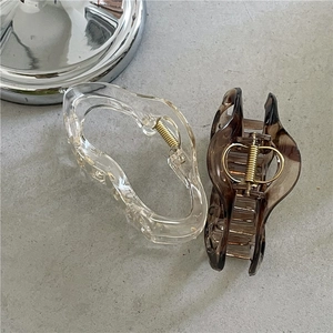 Elegant wavy claw hair clips in clear and amber brown finishes on a grey textured background