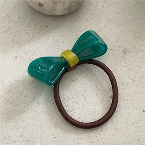 Detailansicht Haargummi mit grüner Azetat-Schleife und gelbem Ring mit Logo-Schriftzug
