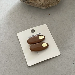 Détail de deux barrettes ovales marron foncé avec pièces métalliques dorées sur carte
