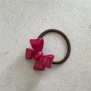 Detail of a bright pink acetate bow hair tie with high-elastic dark brown rope texture