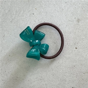 Detail shot of a dark green acetate bow hair tie with a textured brown elastic cord