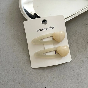Close-up of beige jelly resin heart hair clips on display card over a gray surface