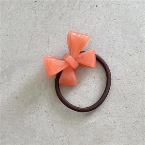 Detailed macro view of coral pink acetate bow hair tie on a grey textured surface