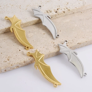 Detailed view of 18k gold and silver bat wing charms on a beige travertine pedestal
