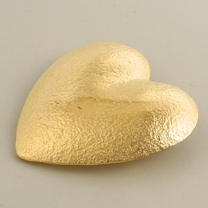 Dettaglio pendente a cuore oro 18k con finitura martellata su sfondo grigio chiaro