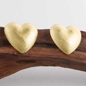Vista macro degli orecchini a cuore 18k con trama martellata su supporto in legno scuro