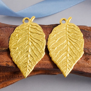 Polished golden stainless steel leaf pendants with detailed veins on dark wood block