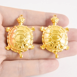Dettagli di due ciondoli a forma di tartaruga dorata con texture a rilievo per gioielli fai da te