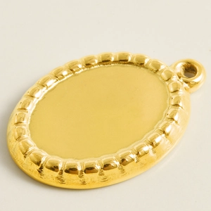 Detailed macro view of an oval 304 stainless steel pendant base with a beaded edge gold finish