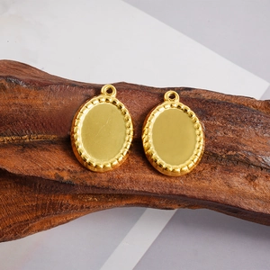 Detail of golden oval pendant bases with beaded edges on a rustic wood surface