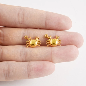 Vue macro de deux pendentifs crabe en or poli de la série océan sur le bout d'un doigt
