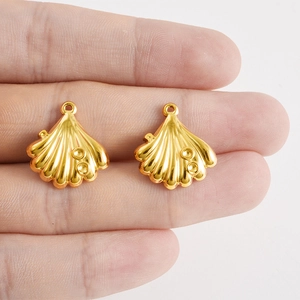 Gros plan de pendentifs coquillages en acier doré avec texture radiale et anneaux de suspension