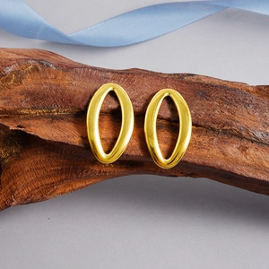 Détail de boucles d'oreilles ovales dorées évidées posées sur une écorce avec rubans