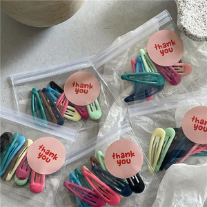 Gros plan d'un lot de 10 barrettes à cheveux gouttes colorées dans un sac cadeau