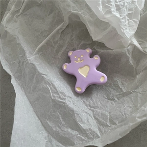 Gros plan d'une pince à cheveux ours violet avec cœur doré sur papier texturé