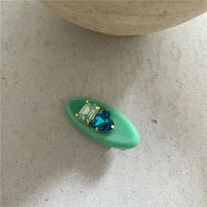 Détail d'une pince à cheveux verte en résine avec strass rectangle jaune et cœur bleu