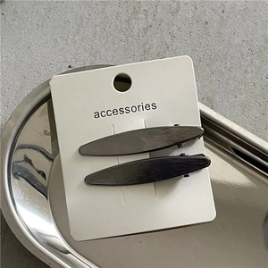 Détail de barrettes à cheveux en métal brossé gris foncé en forme de feuille sur carte