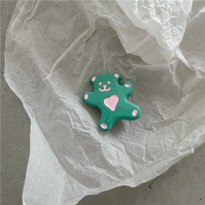 Gros plan d'une jolie pince à cheveux ours en résine verte avec un cœur rose sur papier blanc