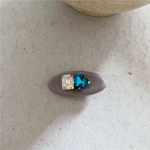 Détail d'une barrette en résine violette avec pierre en cœur bleu et cristal carré