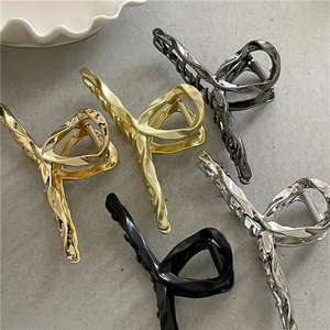 Five assorted liquid metal claw clips in gold, silver and black on stone background