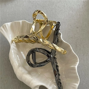 Detail showing polished gold and gunmetal twisted alloy hair claw clips on a tray