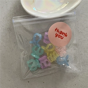 Close-up of ten mini macaron flower hair clips in a transparent thank you gift bag