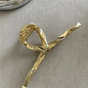Detail of a polished golden alloy hair claw clip with a luxury liquid metal twist design