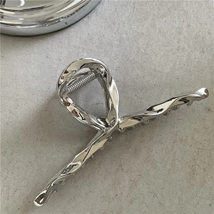 Detail of silver liquid metal hair claw showing anti-slip teeth and sleek fluid design
