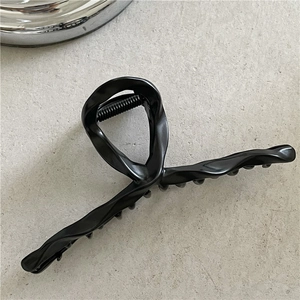 Macro detail of a matte black liquid metal hair claw clip with a twisted streamline design