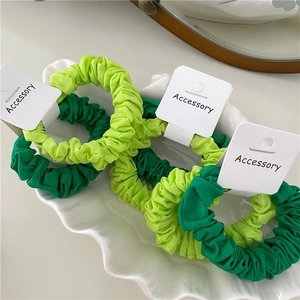 Close-up of light and dark green pleated fabric scrunchies on a shell porcelain dish