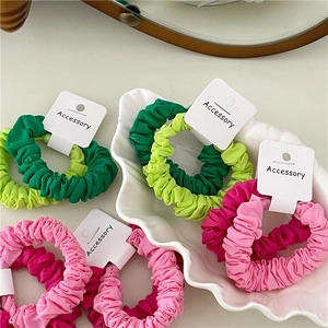Close-up of pleated fabric scrunchies in green and pink on a shell-shaped tray
