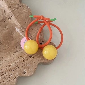 Close-up of orange elastic hair ties with glossy yellow spherical beads on stone tray