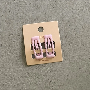 Detail von rosa gewellten Haarspangen auf handgefertigter Karte vor grauem Steinboden
