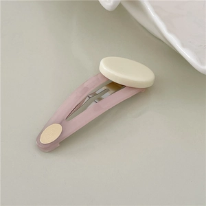 Detailed top view of light pink resin BB hair clip with white oval patch and gold accents