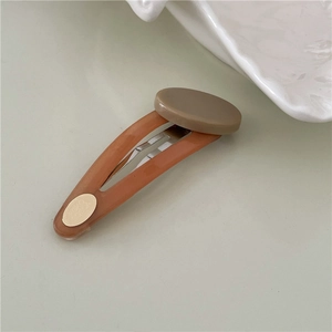 Detail view of oval resin hair clip with contrast color patch and gold metal logo